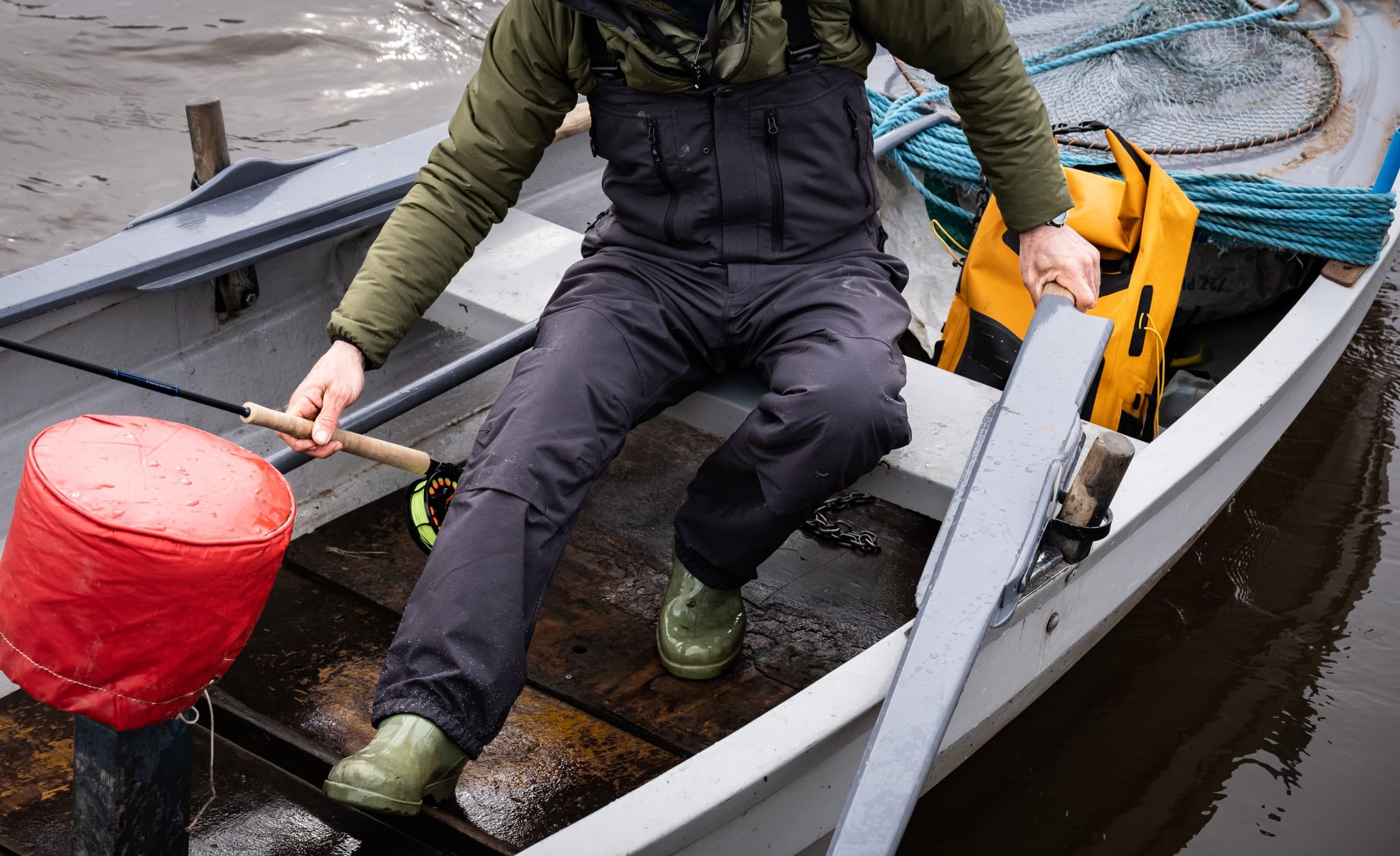 An angler sits in a wet boat wearing the Torne fly fishing bib.